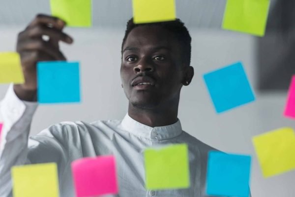 Young afro american business man standing in front of stickers glass wall and write task on sticker at his office place